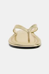 Sandalia plana dorada de cuero, con tira delantera para el dedo y suela delgada.