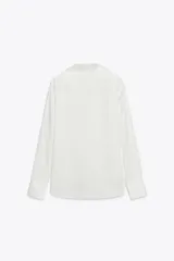 Camisa de mujer satinada color blanco, confeccionada en hilatura con viscosa. Tiene cuello solapa, manga larga con puños y cierre frontal con botones.