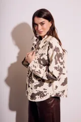 Campera de algodón color crema con estampado de manchas marrones tipo vaca, corte al cuerpo, con cuello clásico, cierre frontal con botones y bolsillos de parche en el pecho.