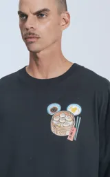 Remera negra de calce oversize, con cuello redondo y un pequeño bordado en el pecho que representa un dim sum (bollo cocido al vapor) en una vaporera de bambú, acompañado de dos platos pequeños y palillos.
