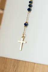 Collar estilo rosario con cadena dorada y cuentas pequeñas de color azul oscuro. Incluye un dije ovalado (medalla) y una cruz colgante en el extremo inferior.