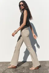 Pantalón de jean color beige, de tiro alto, corte ajustado en la cadera y muslos, y acampanado desde la rodilla. Tiene cinco bolsillos y cierre frontal con cremallera y botón.