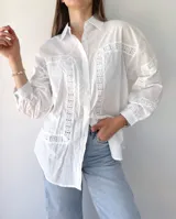 Camisa blanca de mangas largas con detalles de broderie en el frente, mangas y espalda. Corte recto, cuello clásico y cierre frontal con botones.