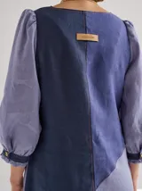 Vestido midi de lino color lila con escote en V y mangas 3/4 abullonadas con puño elástico. Presenta paneles laterales en denim y costuras a la vista en color rojo.