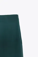 Falda midi verde esmeralda de satén, de tiro alto y corte evasé, con bajo asimétrico y forro interior.