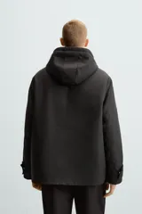 Parka negra de tejido técnico acolchado, corte regular fit, cuello alto con capucha ajustable, manga larga con puños ajustables, bolsillos de solapa en la cadera y bolsillo interior. Cierre frontal con cremallera oculta y botones a presión.
