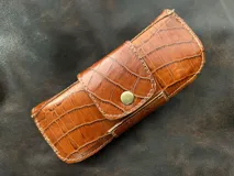 Estuche para lentes color borgoña con textura símil cocodrilo y cierre con broche a presión.