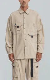 Camisa beige de manga larga, estilo técnica con múltiples bolsillos delanteros y un bolsillo en la parte inferior de la espalda, botones en cartera y mangas, calce oversize, confeccionada en textil ligero suave al tacto.
