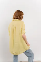 Camisa amarilla de lino con corte recto y calce suelto. Tiene cuello camisero, botones en el frente y mangas cortas con presilla y botón.