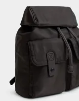 Mochila de tela color lila, con solapa con broche y tira de ajuste, doble bolsillo frontal con broche y pouch con charm lateral en forma de cartera.