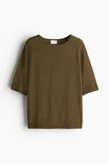 Remera color verde oliva de punto, con corte holgado, cuello redondo y mangas cortas raglán al codo.