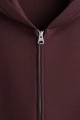 Campera con capucha en tejido efecto neopreno, color borgoña oscuro, con cierre frontal plateado y bolsillos canguro delanteros. Presenta un corte holgado y hombros caídos.