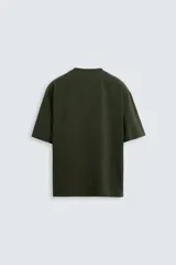 Camiseta verde oscuro de corte holgado, confeccionada en tejido de algodón grueso. Tiene cuello redondo y mangas cortas sin costura en la sisa.