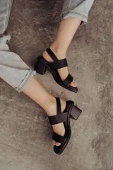 Sandalia de cuero color negro con taco bloque medio y punta cuadrada. Presenta dos tiras anchas sobre el empeine, una de ellas con hebilla metálica dorada, y una tira de sujeción en el talón. Posee base acolchonada para mayor comodidad.