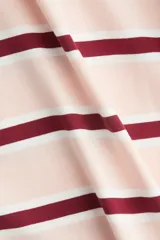 Remera de manga tres cuartos con cuello redondo, hombros caídos y corte holgado. Presenta un patrón de rayas horizontales en tonos rosa pálido, blanco y granate.
