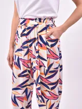 Pantalón babucha de tela estampada con hojas en tonos rosa, naranja y azul, con cintura elastizada y lazo para ajustar.