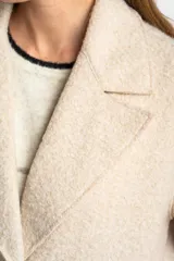 Tapado largo color beige claro, de corte oversize, con cuello solapa y cierre frontal de botones.