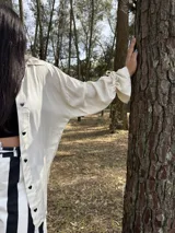 Camisa oversize de fibrana color crudo con botones negros en forma de corazón y mangas largas con puños elásticos.