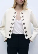 Chaqueta corta color crema con cuello redondo y detalles troquelados.
