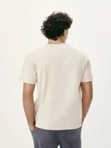 Camiseta blanca de algodón con cuello redondo y mangas cortas. Estampa rectangular con borde negro que contiene la frase "NATURAL ATMOSPHERE" en letras mayúsculas y una imagen de montañas y mar.