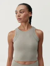 Top deportivo color gris con perforaciones decorativas en la parte delantera y trasera. Tejido Shape_Tech con tecnología performance, de sujeción media-alta, con copas extraíbles.