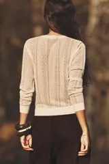 Chaqueta color crema de tejido de punto calado, con cuello redondo, manga larga y cierre frontal con botones.
