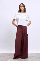 Remera blanca de algodón con cuello redondo y mangas cortas. Presenta apliques metálicos y aberturas circulares en los hombros y el frente.