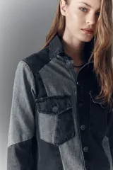 Campera recta de denim rígido negro con recortes en gris. Tiene bolsillos con solapa y botones metálicos.