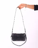 Bandolera marrón de cuero con tachas plateadas y correa de cuero con tachas plateadas. Tiene dos asas desmontables, una corta con tachas para llevarla en la mano o al hombro y una larga para llevarla al hombro o cruzada.