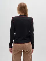 Polera negra de tela rib con cuello alto y mangas largas. Presenta pespuntes rojos en cuello, hombros y puños.