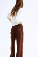 Pantalón ancho color marrón chocolate, de tiro alto con elástico en la parte posterior de la cintura y cierre oculto con corchete en un lado. Presenta bolsillos laterales discretos y piernas amplias con pliegues adelante y atrás.