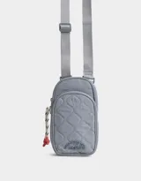 Portacelular gris acolchado de tela deportiva con bolsillo frontal con cierre y puller de goma. Tiene correa regulable y desmontable y cierre superior.