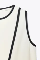 Blusa blanca sin mangas de crepe con cuello redondo y detalle de ribete negro en cuello, sisas y abertura frontal diagonal.