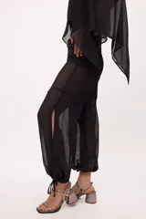 Pantalón negro traslúcido con corte ancho y ajuste en los tobillos.