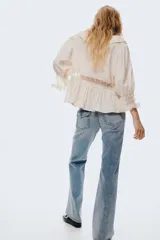 Jeans de denim azul claro con efecto lavado y desgaste sutil. Tienen un corte ajustado hasta la rodilla y luego se abren en un estilo acampanado (flare). Son de tiro bajo y presentan bolsillos delanteros abiertos y bolsillos traseros con solapa y botón.