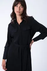 Vestido camisero midi negro con cuello camisero, mangas largas, dos bolsillos en el pecho, cinturón de lazo y abertura lateral.