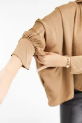 Camisa color beige de satén con corte holgado, cuello camisero y mangas largas con puños abotonados.