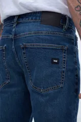 Jean de denim azul oscuro, corte slim fit, entallado en caderas y muslos, ajustado levemente desde la rodilla hasta el tobillo.