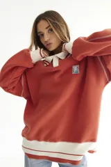 Buzo celeste con cuello polo y puños en rib color verde lima. Tiene un parche con el logo de la marca en el pecho y rayas horizontales en el ruedo.