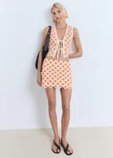 Top de crochet color crudo con flores naranjas, sin mangas, con escote en V y cierre frontal con lazos.