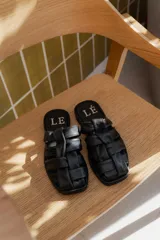 Sandalias tipo mule de cuero color marrón chocolate, con diseño de tiras anchas cruzadas y suela plana.