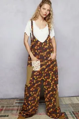 Mono oversize con tirantes finos y escote en V, decorado con estampado floral en tonos marrones, naranjas y amarillos. Presenta bolsillos frontales con apliques de diferentes texturas y patrones.