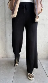 Pantalón negro de tejido de punto acanalado, corte palazzo, cintura alta con cordón ajustable y aberturas con cierre en los tobillos.