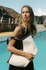 Bolso tipo shopper color crudo, con cuerpo de lona y detalles en cuero marrón. Tiene doble asa de hombro y una bolsa interior extraíble con cierre de cremallera. Se cierra con un lazo.