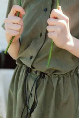 Vestido corto verde militar de microfibra con cuello camisero negro, cintura elastizada con cordón de ajuste y mangas cortas con dobladillo. Cierre frontal con botones.