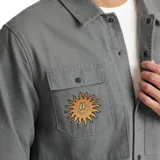 Campera gris de algodón canvas, estilo camisa, con bordado de un sol en el bolsillo del pecho. Tiene dos bolsillos con solapa en el pecho y cierre con botones. Corte recto y holgado.