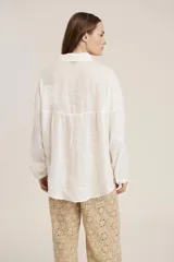 Camisa blanca de manga larga, corte holgado, con cuello camisero y detalles de bordados perforados (calado) verticales en el frente.