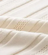 Camisa de punto color crema, con cuello polo y cierre frontal parcial con cremallera, de manga corta y diseño texturizado con perforaciones verticales.