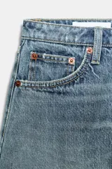 Shorts de jean de algodón, tiro alto, color azul claro desgastado. Presenta cinco bolsillos, cierre frontal con botón metálico y bajo desflecado con vuelta.