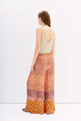 Pantalón amplio de viscosa y modal con cintura elastizada. Presenta un estampado batik en tonos naranja, terracota y morado, con textura plisada y apliques de lentejuelas circulares plateadas.